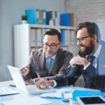 Two men in suits discussing IT Consulting services on a laptop screen.