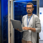 A man in a server room holding a laptop, providing Managed IT Services.